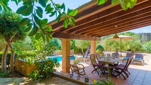 An outdoor patio area with a wooden pergola, a pool, and seating arrangements.