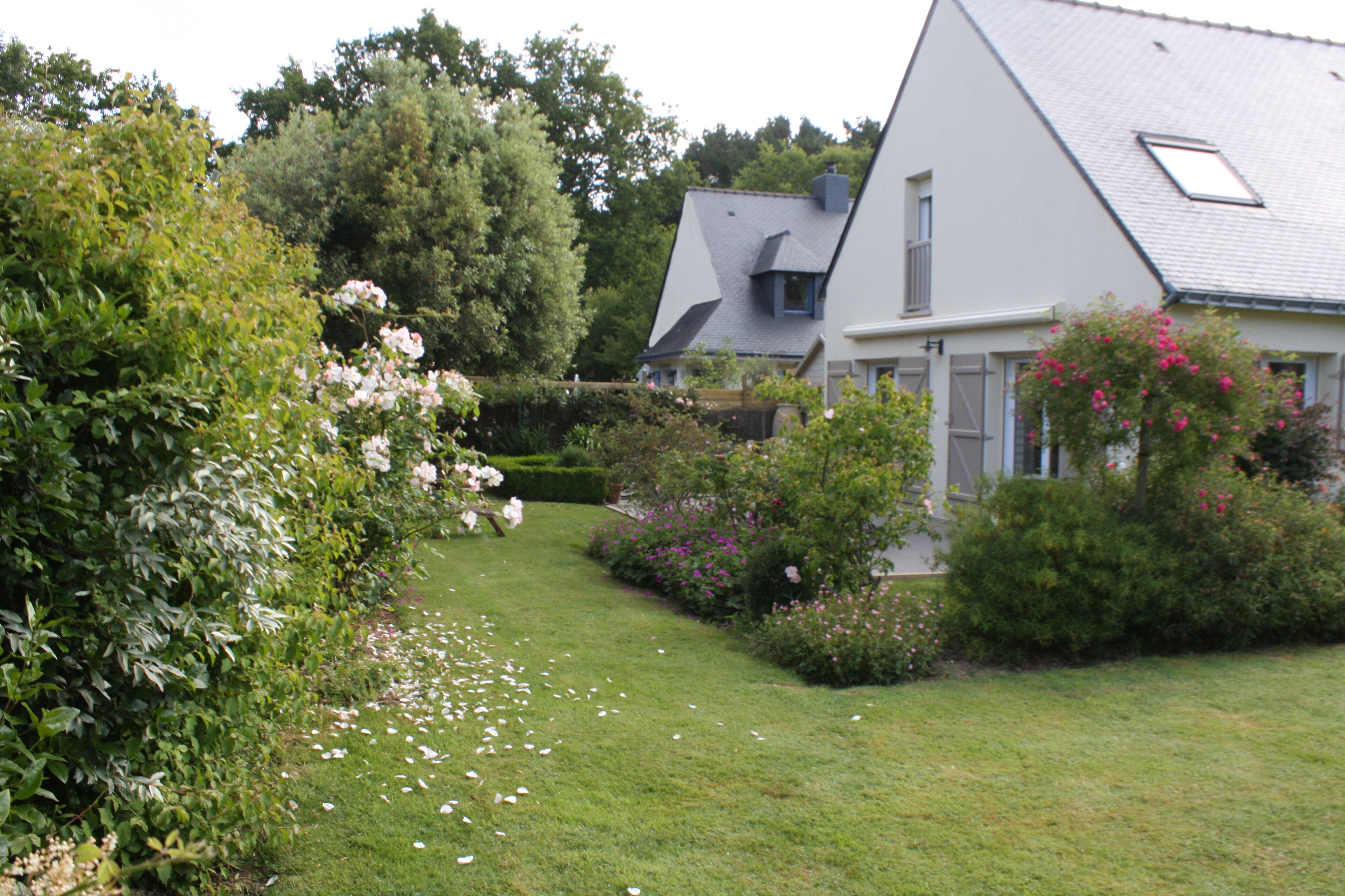 A house with a sloped roof, surrounded by lush greenery and flowering plants.