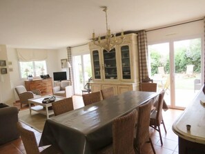 A spacious living room with a dining table, chairs, a television, and a cabinet.