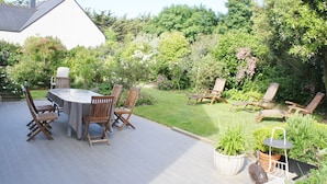 Een terras met een tafel en stoelen, omringd door weelderige begroeiing en een wit gebouw op de achtergrond.