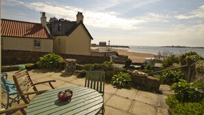 A patio with a table and chairs, overlooking a beach and the sea.