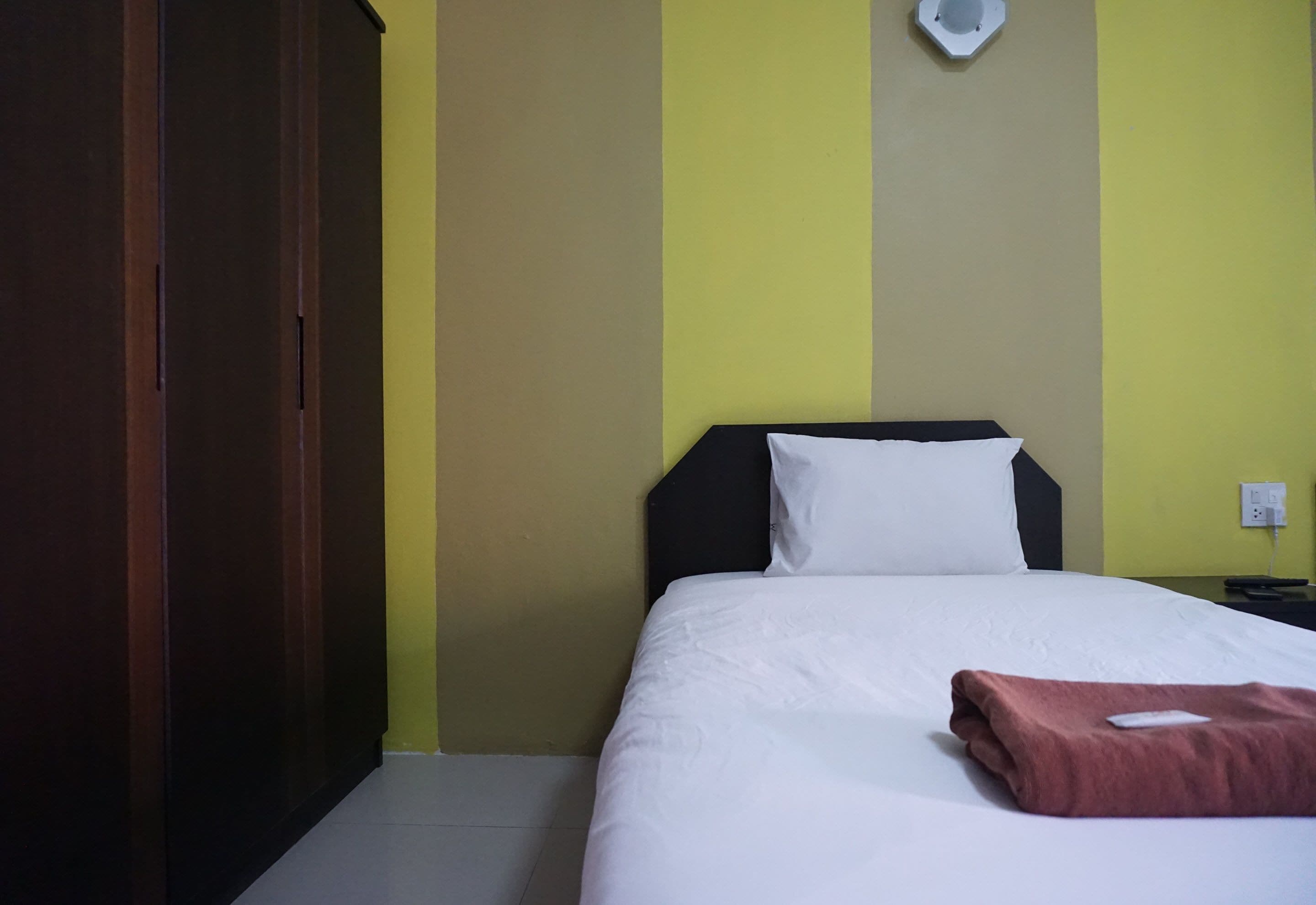 Una habitación de hotel con una cama, un armario de madera y una pared con una lámpara.
