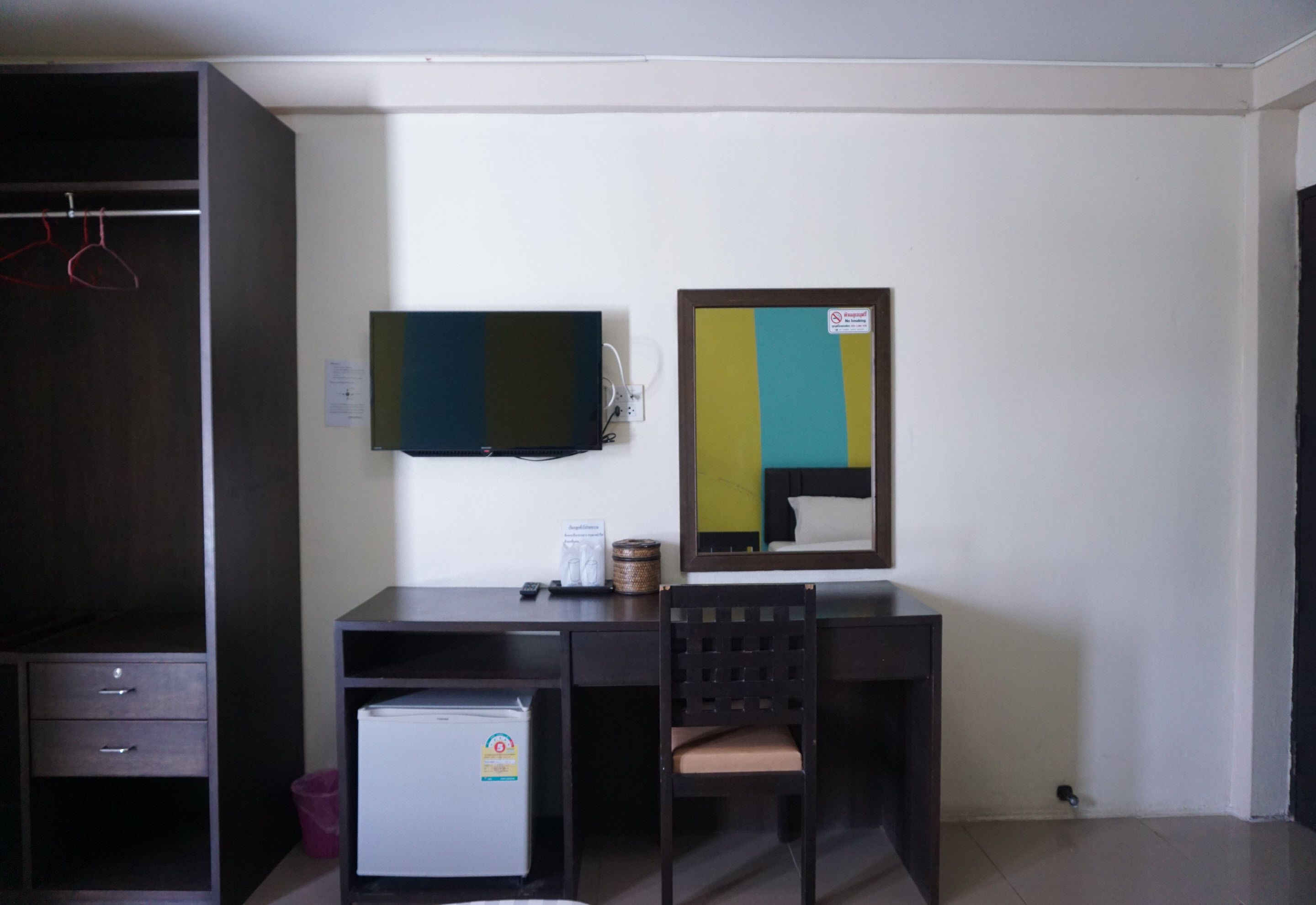 Une pièce avec un bureau en bois foncé, un petit réfrigérateur, une chaise, un téléviseur et un miroir au mur.