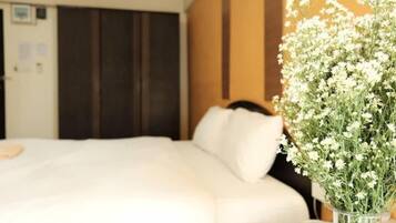 A hotel room with a bed, a bedside table, and a vase with white flowers.