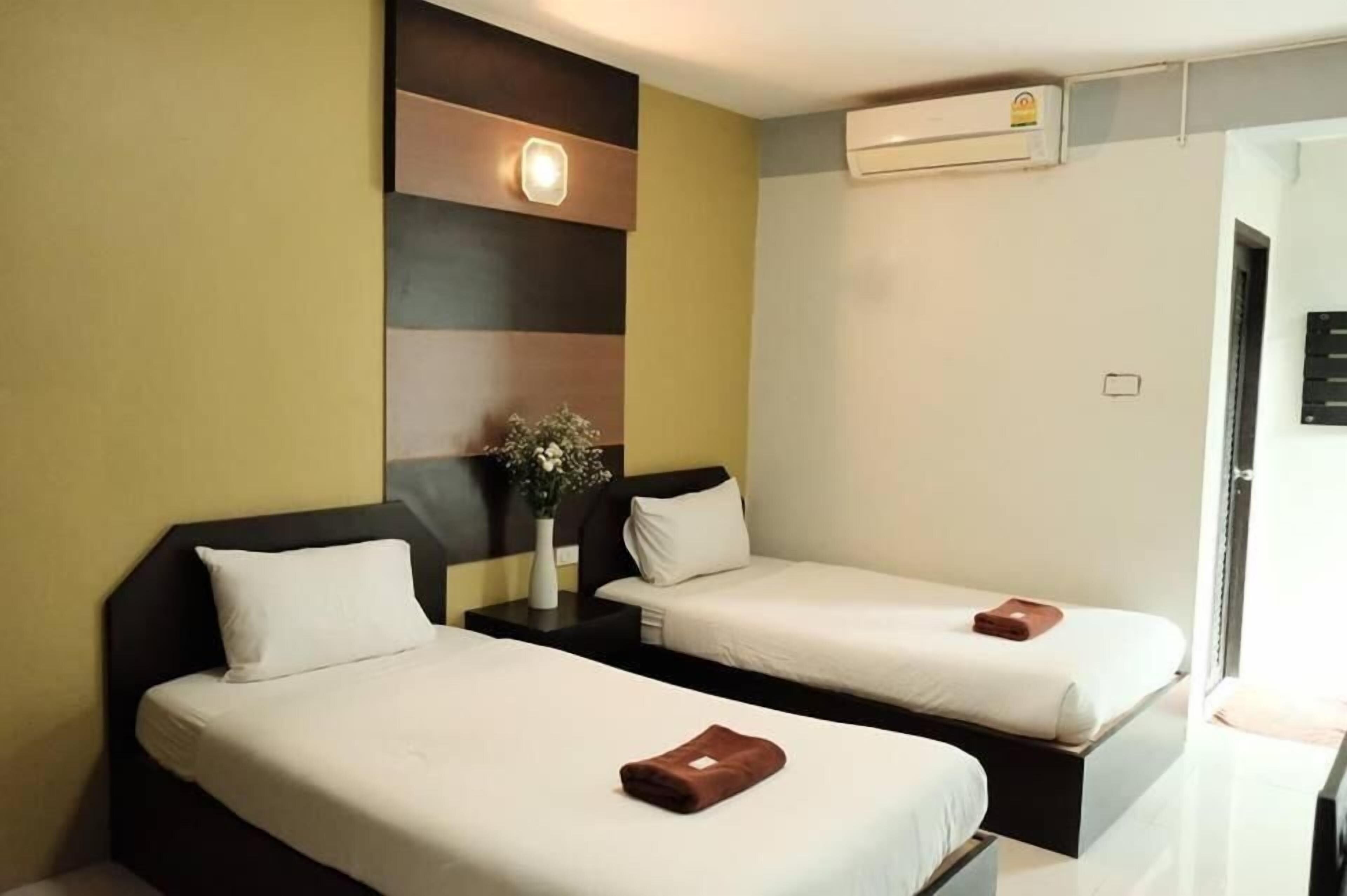 Habitación de hotel con dos camas individuales, una mesita de noche con un jarrón de flores y un equipo de aire acondicionado en la pared.