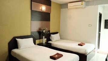 Habitación de hotel con dos camas individuales, una mesita de noche con un jarrón de flores y un equipo de aire acondicionado en la pared.