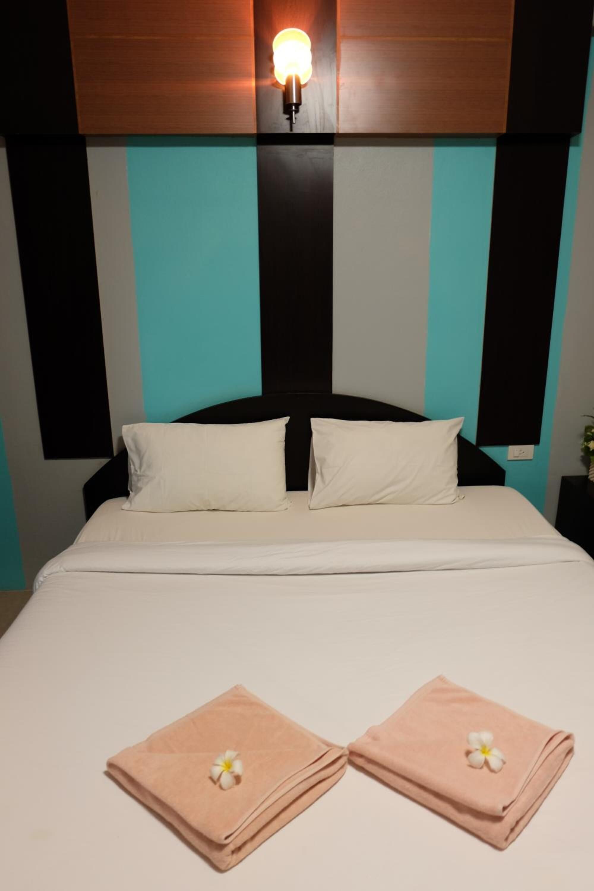 Habitación de hotel con cama, dos almohadas, mesita de noche y lámpara de pared.