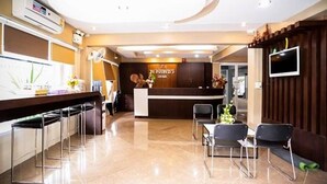 A hotel reception area with a modern design, featuring a reception desk, seating area, and a TV mounted on the wall. - Puangpech Place (Lampang)