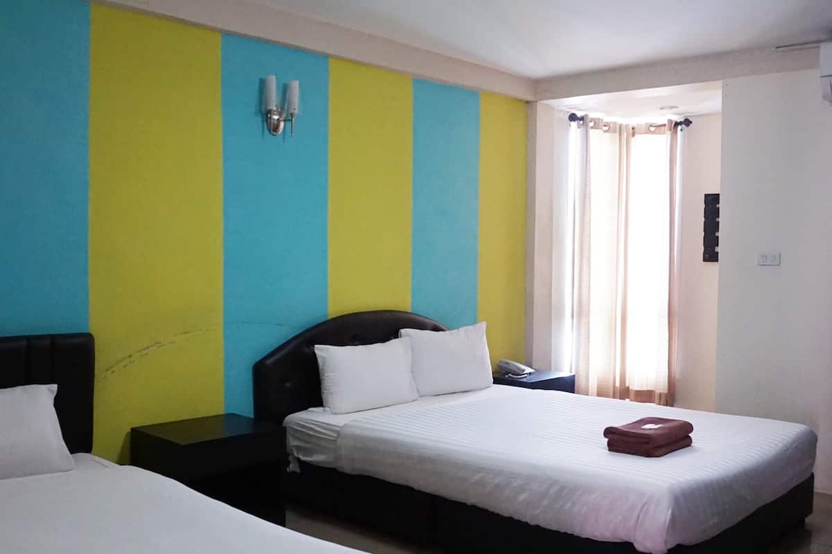 A hotel room with two beds, a nightstand, a wall-mounted lamp, and a window with curtains.