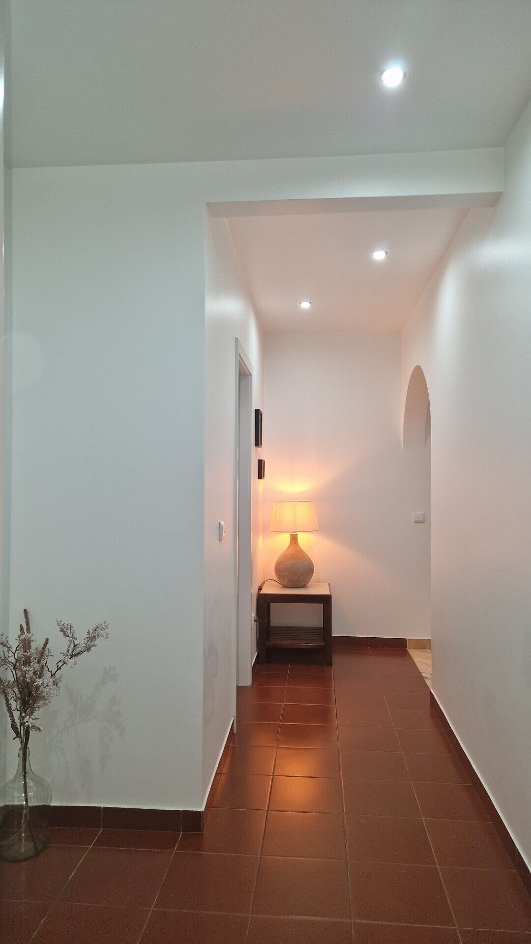 A hallway with a lamp, a vase with flowers, and a door.