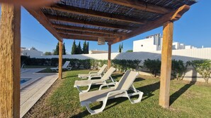 A covered outdoor seating area with wooden posts and a thatched roof, surrounded by a pool and a well-maintained lawn. - Luxury villa, with garden and private pool, A/C, free WiFi, near beach (Albufeira)