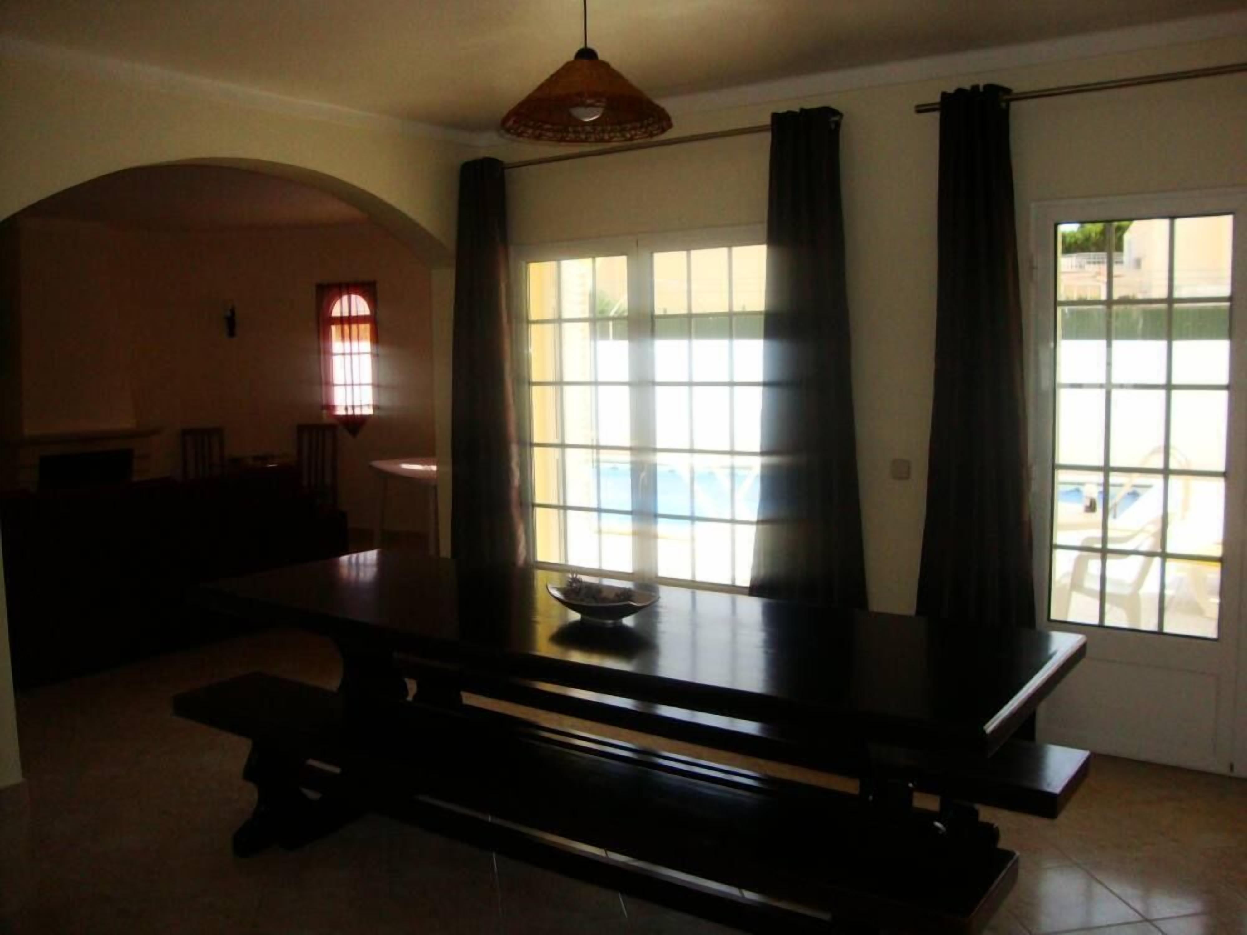Un comedor con una mesa y bancos, una ventana con cortinas y vistas al exterior.