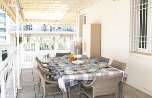 Ein überdachter Essbereich im Freien mit Korbstühlen und einem für eine Mahlzeit gedeckten Tisch, mit Blick auf einen Balkon mit Geländern.