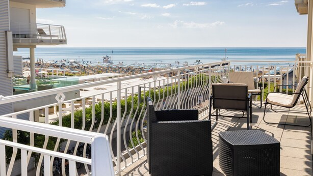 Un balcon aménagé avec du mobilier d’extérieur, une piscine et une vue sur la plage et l’océan.