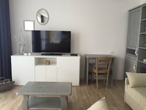 A living room with a flat-screen TV on a white cabinet, a wooden chair, a small table, and a sofa.