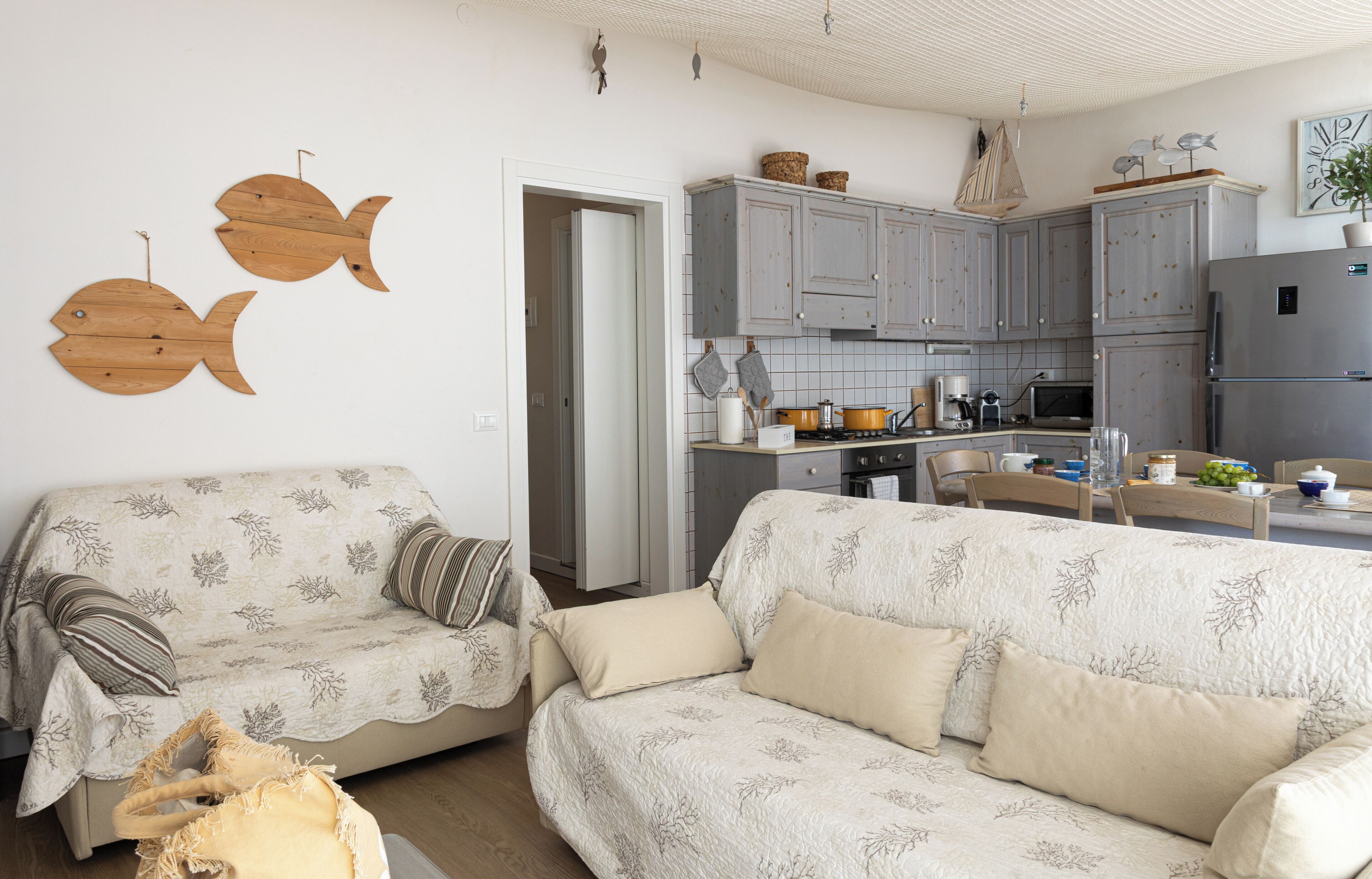 A living room with two sofas, a coffee table, and a kitchen with grey cabinets and a refrigerator.