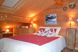 A cozy wooden cabin bedroom with a bed, two nightstands, a dresser, and a framed picture on the wall.
