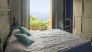 A bedroom with a bed, two pillows, a wardrobe, and a view of the sea.