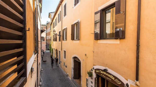 A narrow street with buildings on either side, a visible shop with a sign, and a dog walking on the cobblestone path.