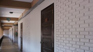 A corridor with white brick walls, a dark wooden door, and a ceiling light fixture. - Puangpech Hotel (Lampang)