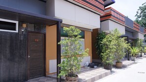 A modern building with a dark brown door labeled "107," a checkered tiled walkway, and several potted plants along the side. - Puangpech Hotel (Lampang)