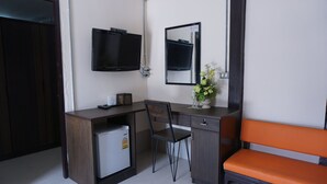 A hotel room with a desk, chair, small refrigerator, TV, mirror, and an orange bench. - Puangpech Hotel (Lampang)