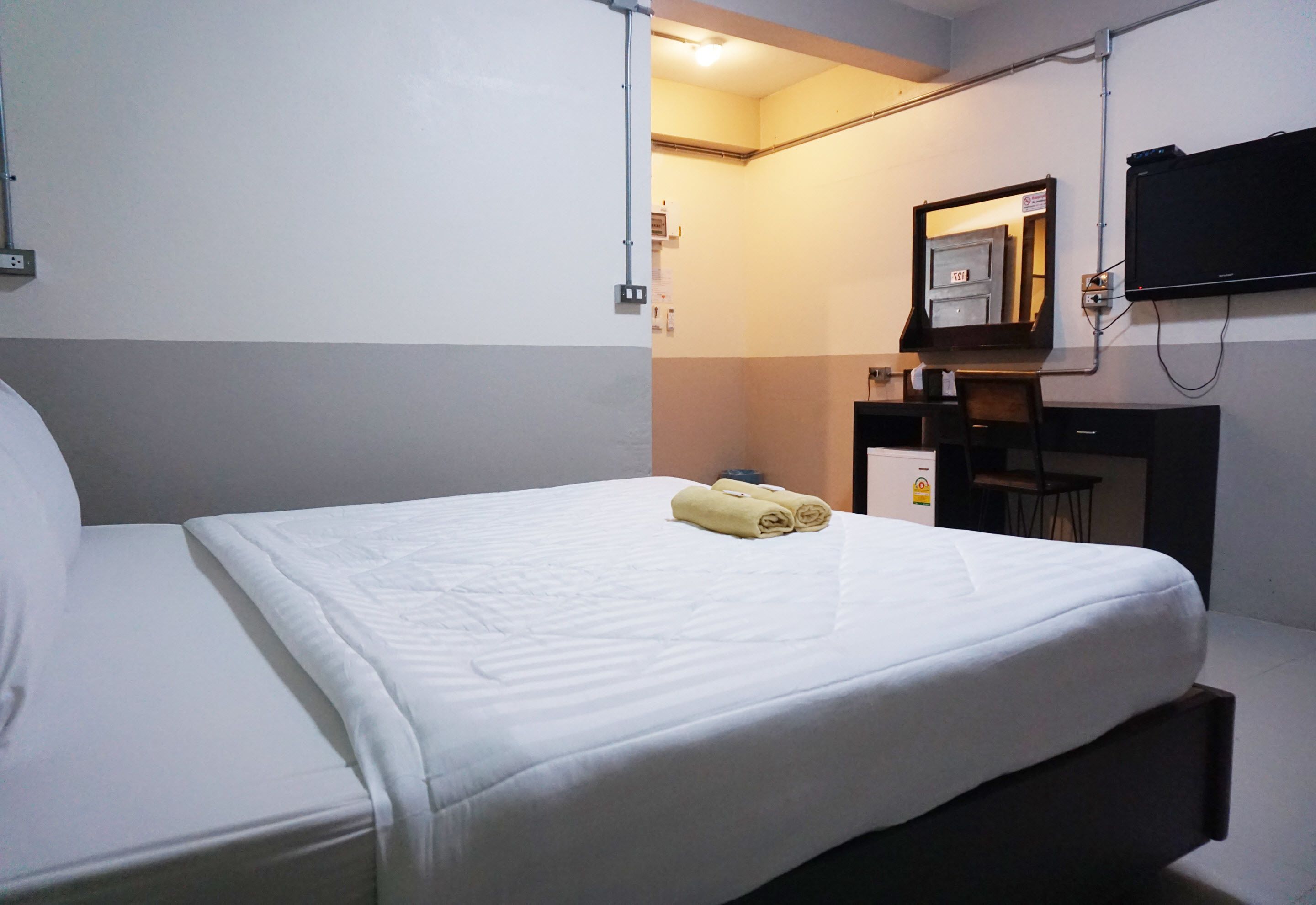 A hotel room with a bed, a desk, a chair, a TV mounted on the wall, and a mirror above the desk.