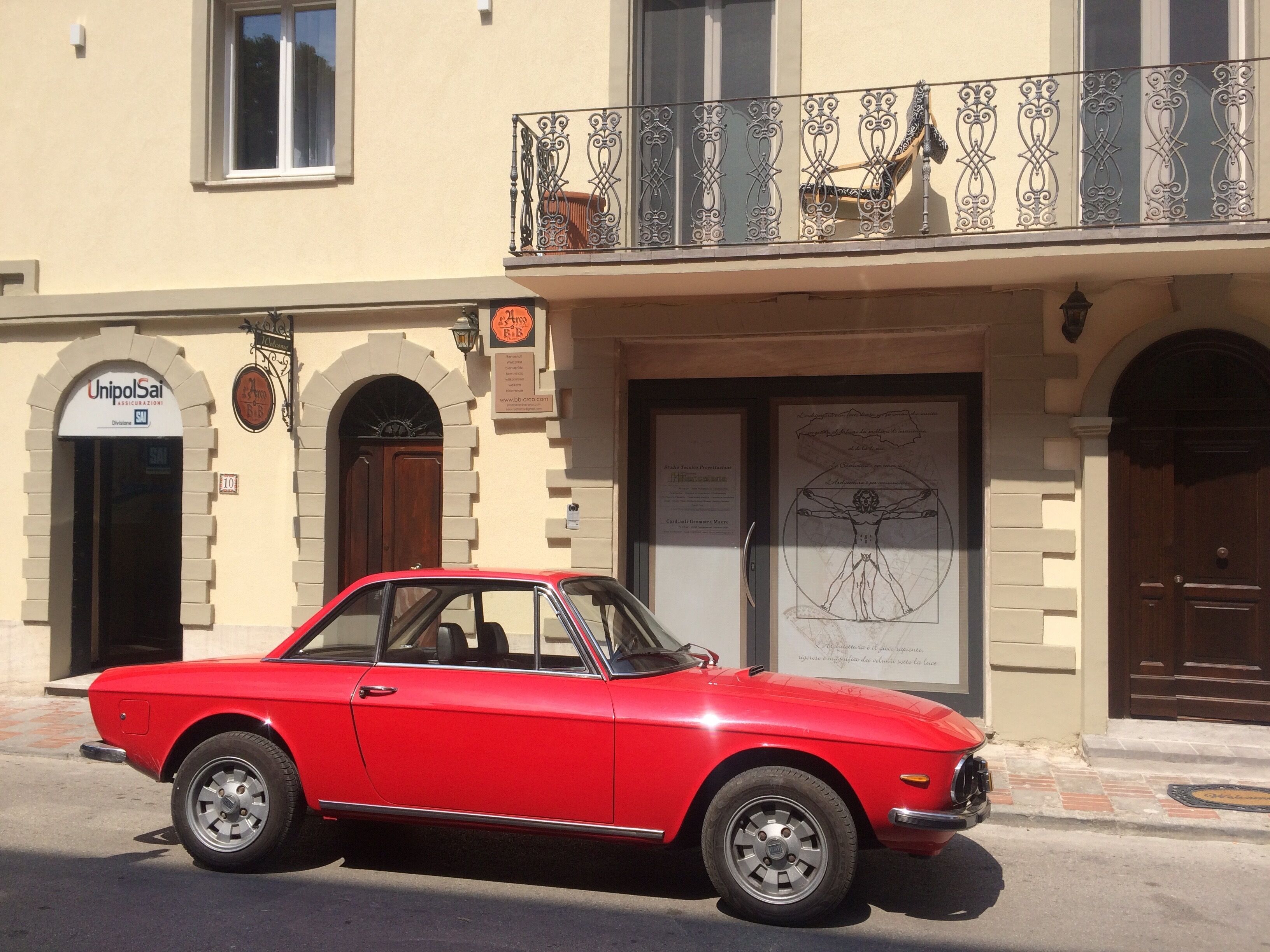 A red vintage car parked in front of a building with a sign reading "UnipolSai".