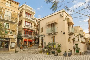 Ein traditionelles Gebäude im mediterranen Stil mit einer Steinaußenfassade, mehreren Balkonen und einem schachbrettartigen Pflaster vor der Tür.