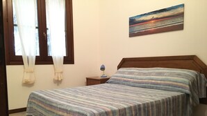 A bedroom with a bed, a nightstand, a lamp, and a painting on the wall. - Terraced house in the shade of pine trees 500 meters from the beach.   (PULA)