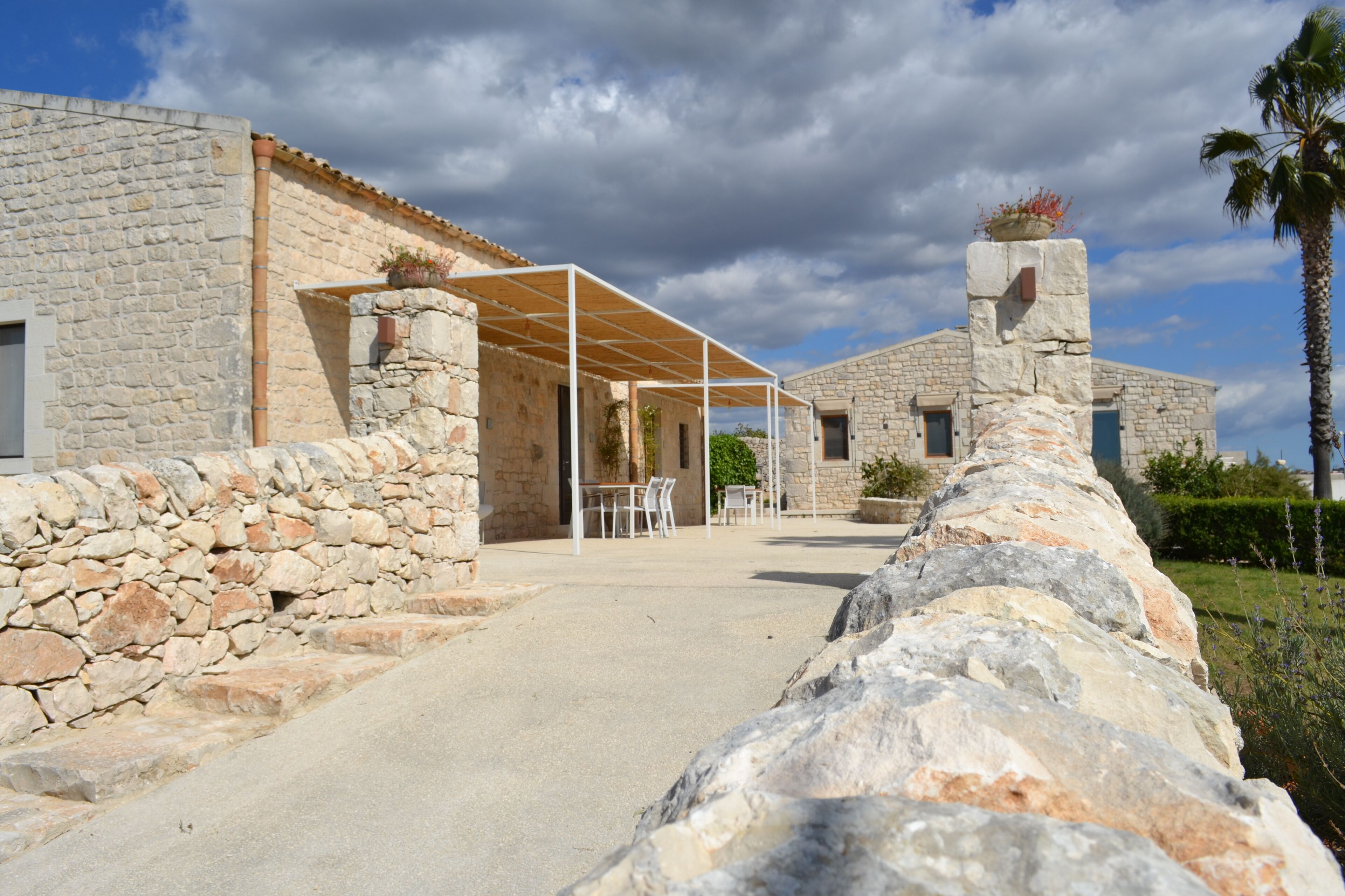 A stone building with a covered patio area, stone walls, and a palm tree.