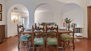 Un comedor con una mesa y sillas de madera, una araña y una estantería.