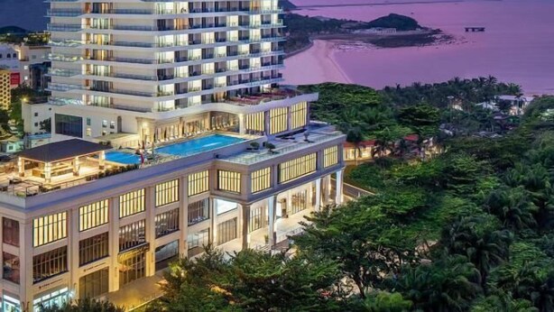 Um hotel moderno com várias varandas, piscina no terraço e vista para o mar.