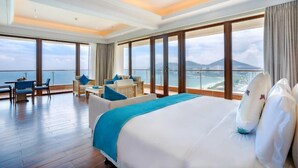 Quarto de hotel espaçoso com uma cama grande, varanda com vista para o mar e área de estar com mesa e cadeiras.