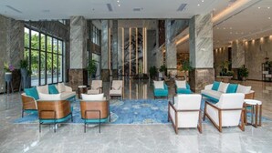 Um hall amplo com piso de mármore, mobiliário moderno e grandes janelas com vista para áreas verdes.