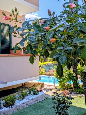 Un jardin avec une piscine, un rosier et un bâtiment doté d’un balcon.