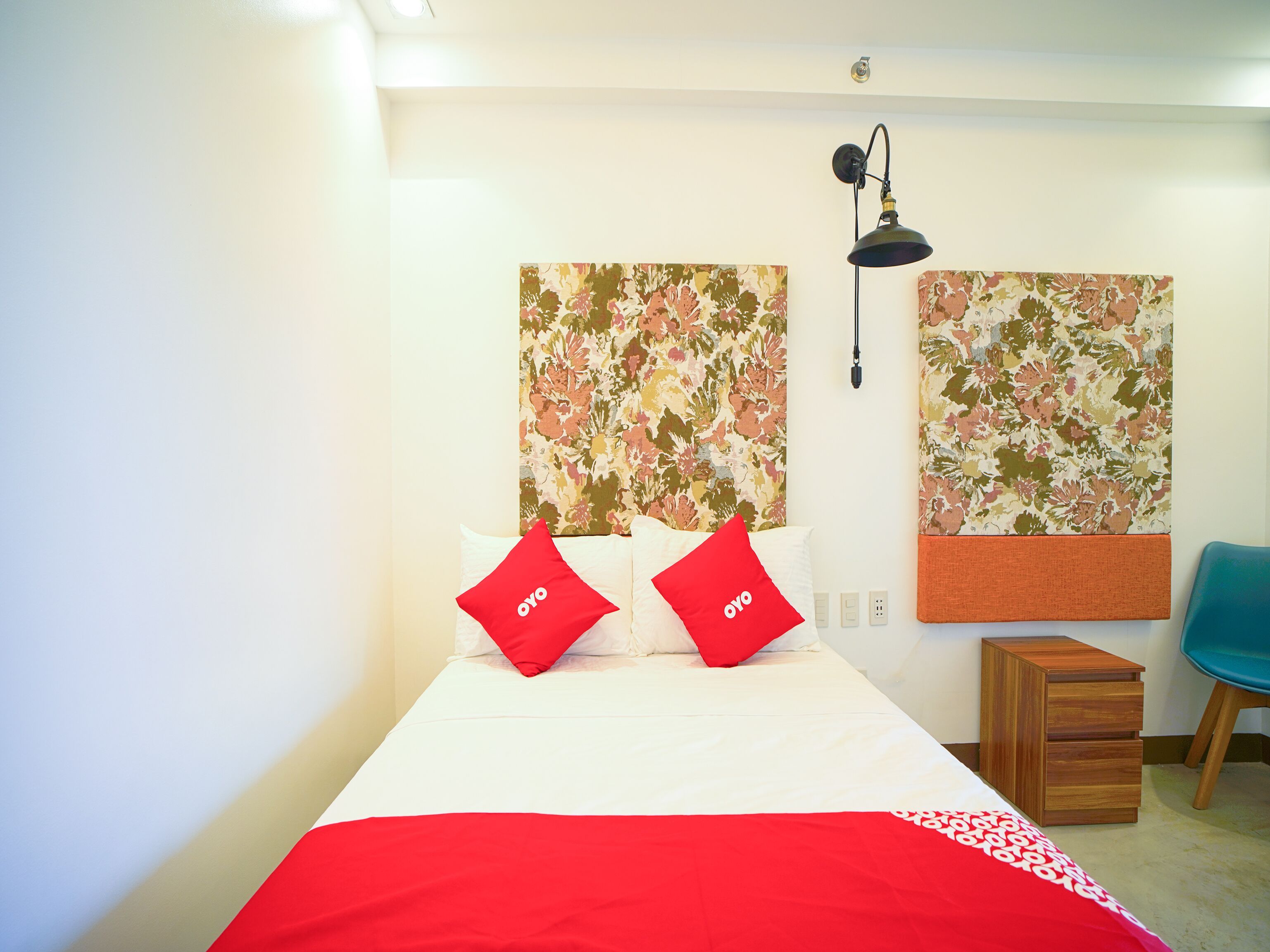 A neatly arranged hotel room with a bed, two red pillows, a wooden nightstand, a desk, and a chair.