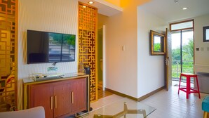 A modern living room with a flat-screen TV, wooden cabinet, glass coffee table, and a red stool. - Capital O Vaccinated Staff - OYO 785 The Greenhive (Ibaan)