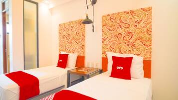 A hotel room with two beds, each with red and white bedding, and a patterned wallpaper on the walls.