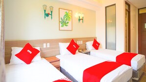 A hotel room with three beds, each with a red pillow and white bedding. There are wall-mounted light fixtures and a framed plant on the wall. - Capital O Vaccinated Staff - OYO 785 The Greenhive (Ibaan)