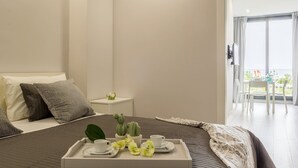 Ein Hotelzimmer mit Bett, Nachttisch und einem Tablett mit Frühstücksangeboten, mit Blick auf das Meer vom Balkon aus.