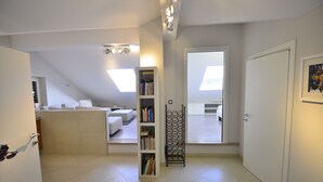 Una habitación moderna y bien iluminada, con tragaluces, una estantería y una puerta que da a otra habitación.
