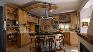 Una cocina moderna con armarios de madera, una isla central con taburetes de bar y una campana extractora de acero inoxidable.