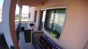 A balcony with a grill, a small table, and a window with a view of buildings. - Quinta do Anjo Apartment (Palmela)
