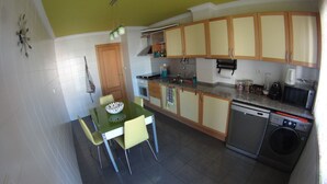 A compact kitchen with a dining table, chairs, a sink, a stove, and a dishwasher. - Quinta do Anjo Apartment (Palmela)