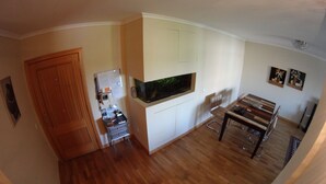 A compact living space with a wooden door, a small desk with a computer, a mounted aquarium, and a dining area with a table and chairs. - Quinta do Anjo Apartment (Palmela)
