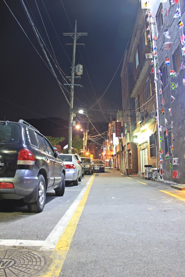 A street lined with parked cars and buildings with flags.