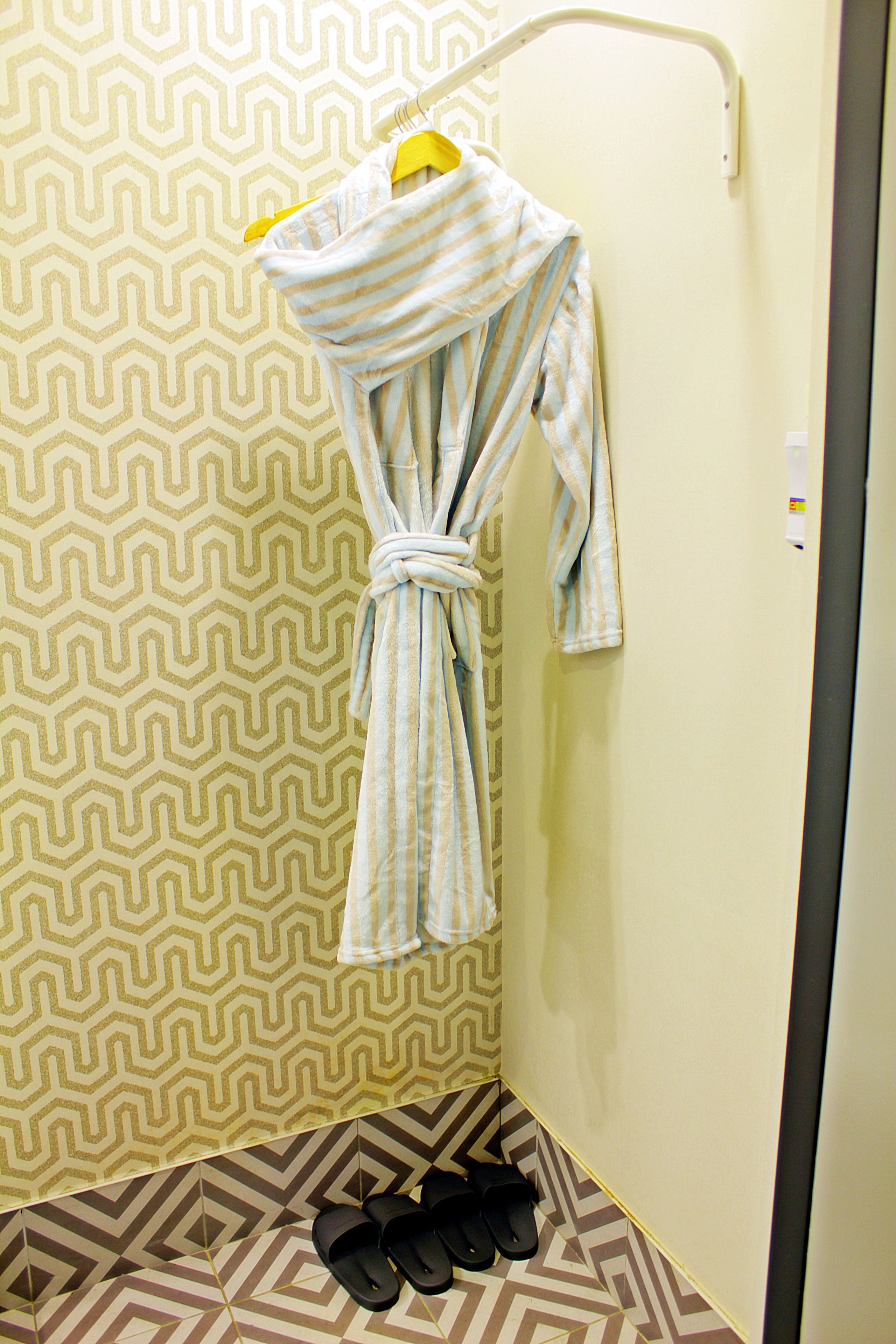 Un baño con pared estampada, un perchero con toalla y un par de pantuflas en el suelo.