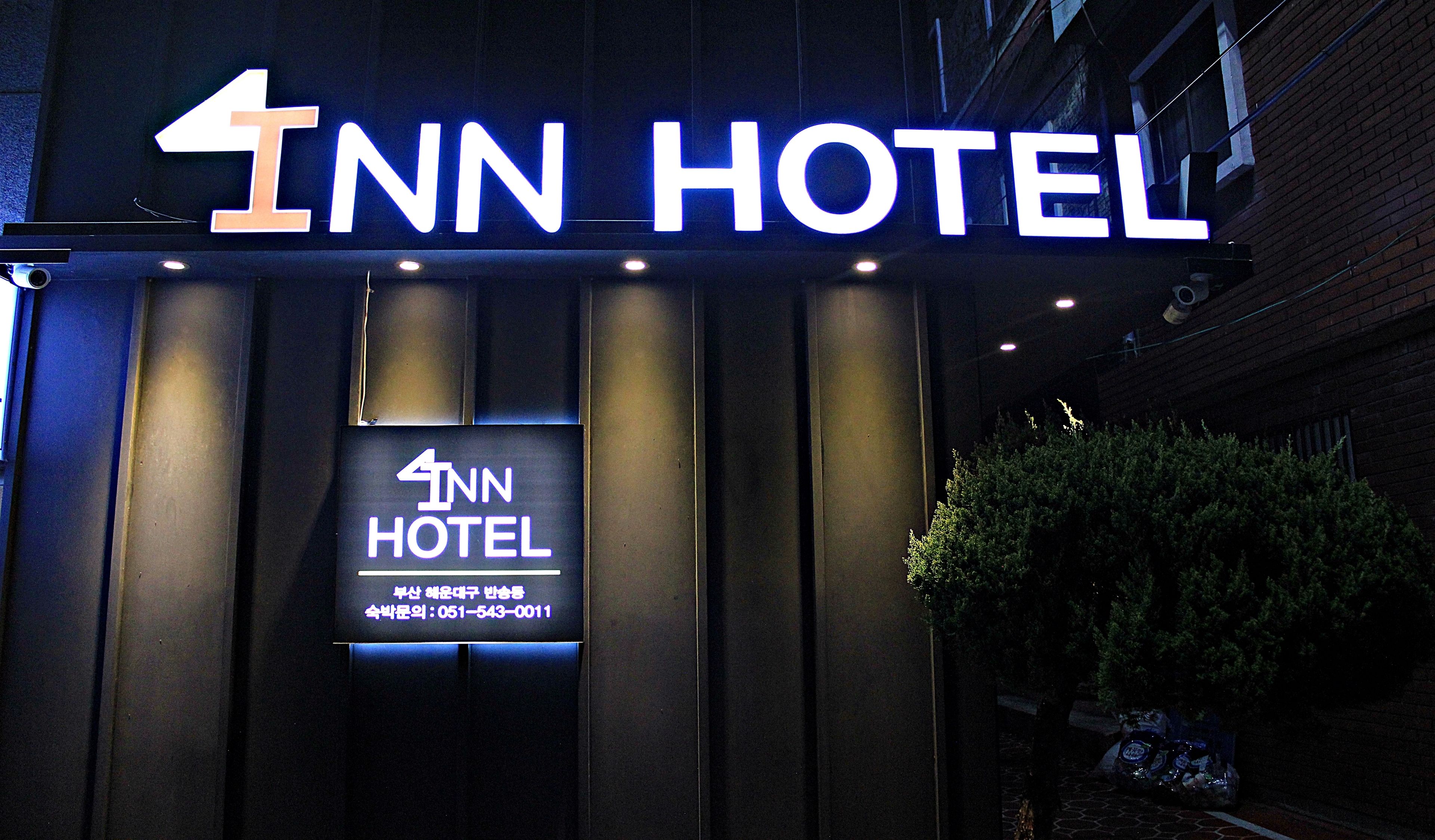 Entrada d'hotel amb un cartell destacat que mostra el nom "4INN HOTEL" i un cartell més petit a sota amb informació de contacte.