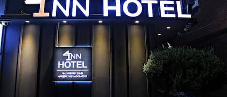 A hotel entrance with a prominent sign displaying the name "4INN HOTEL" and a smaller sign below with contact information.